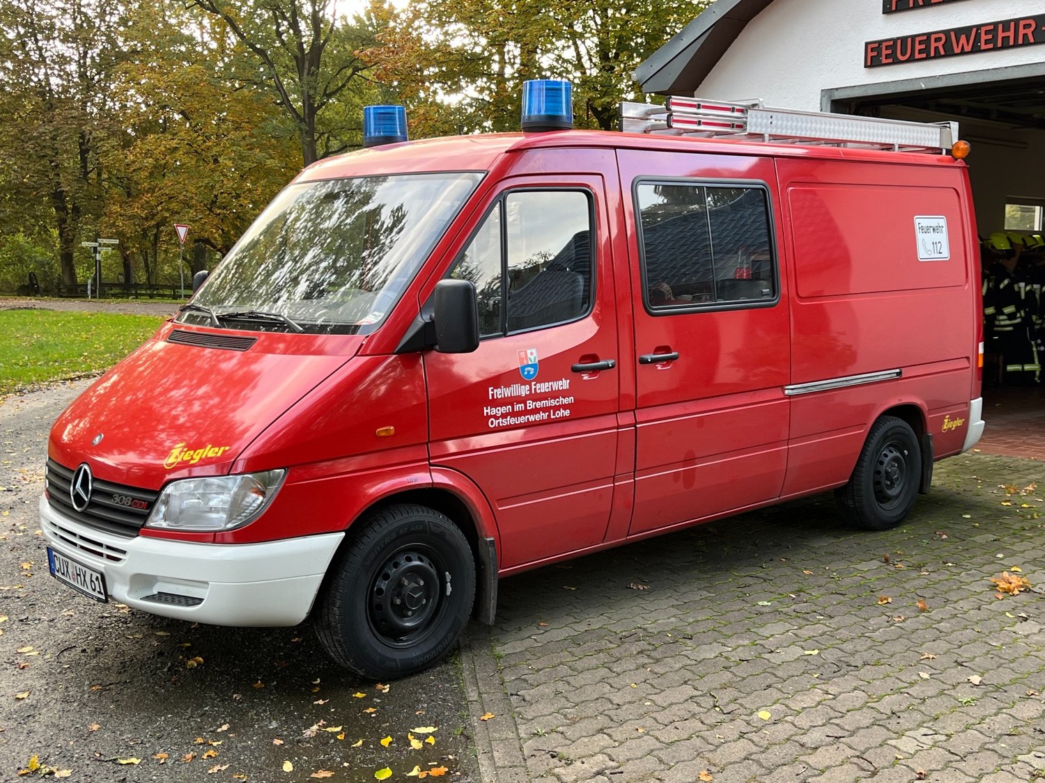 Rotes Feuerwehrfahrzeug der Ortsfeuerwehr Lohe vor dem Feuerwehrhaus